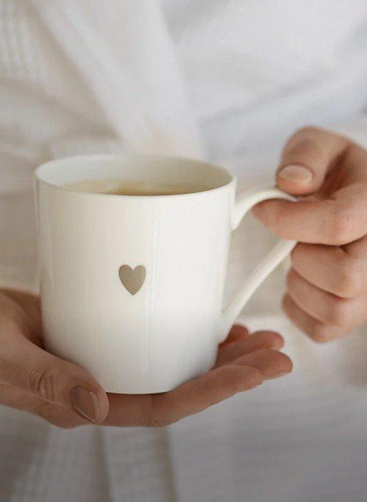 a person holding a white mug with a heart on it