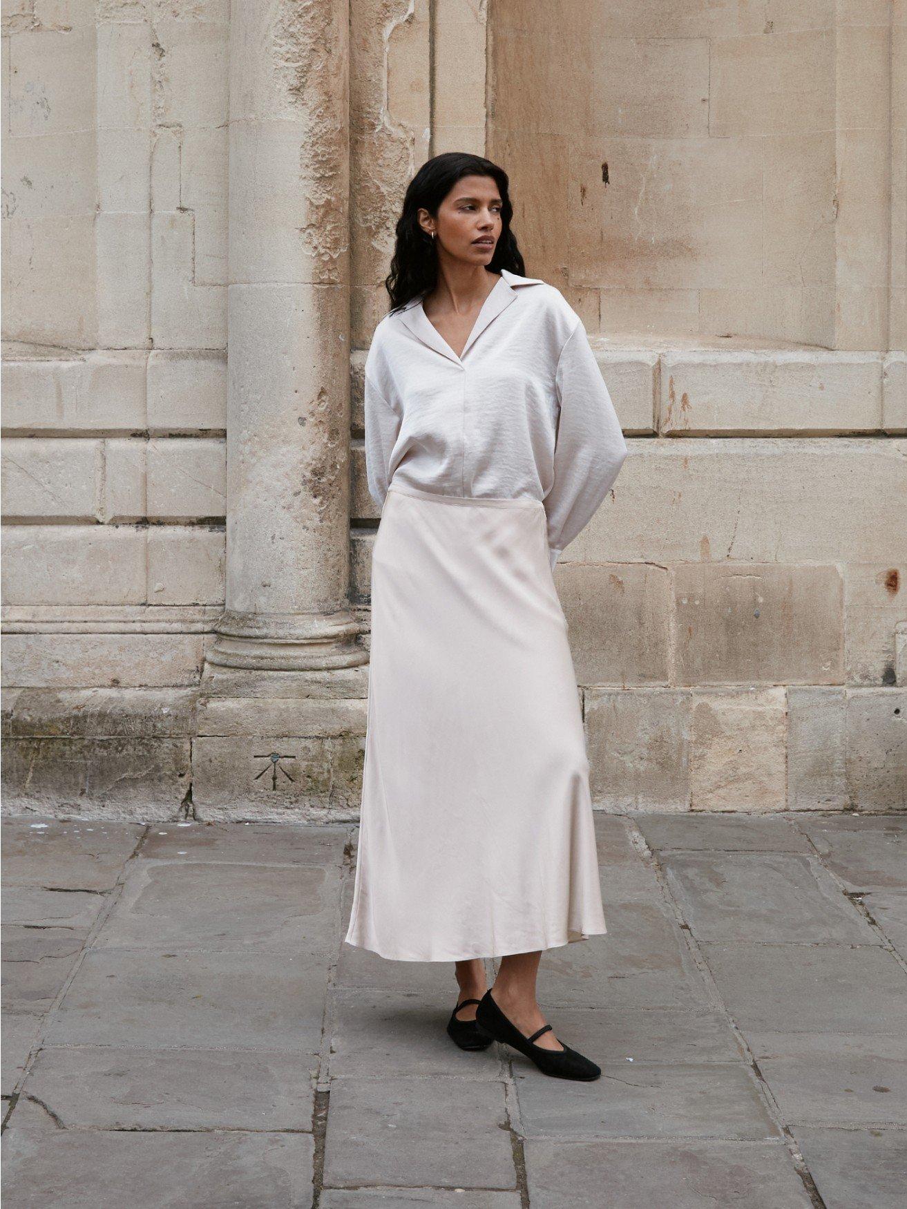 a woman in a white shirt and skirt standing in front of a building