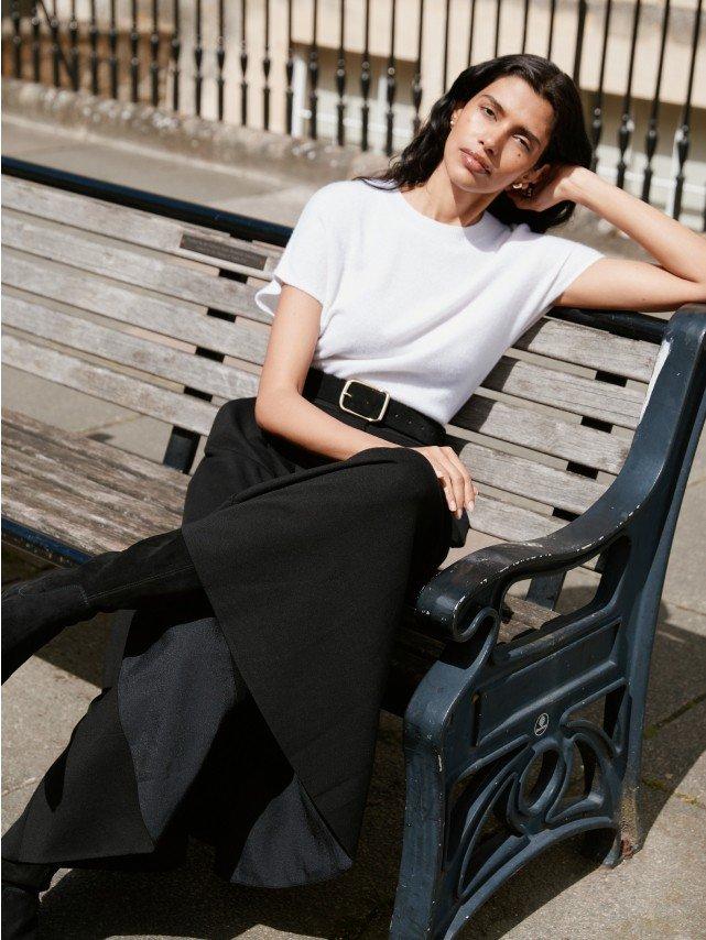 a woman in a white shirt and black skirt sitting on a bench