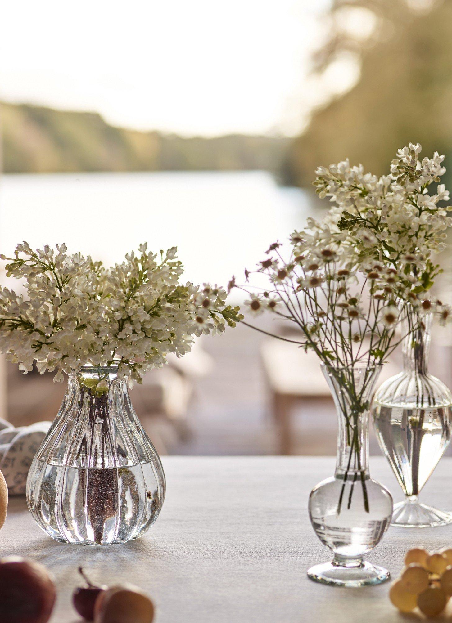 three vases of flowers on a table with a view of the water