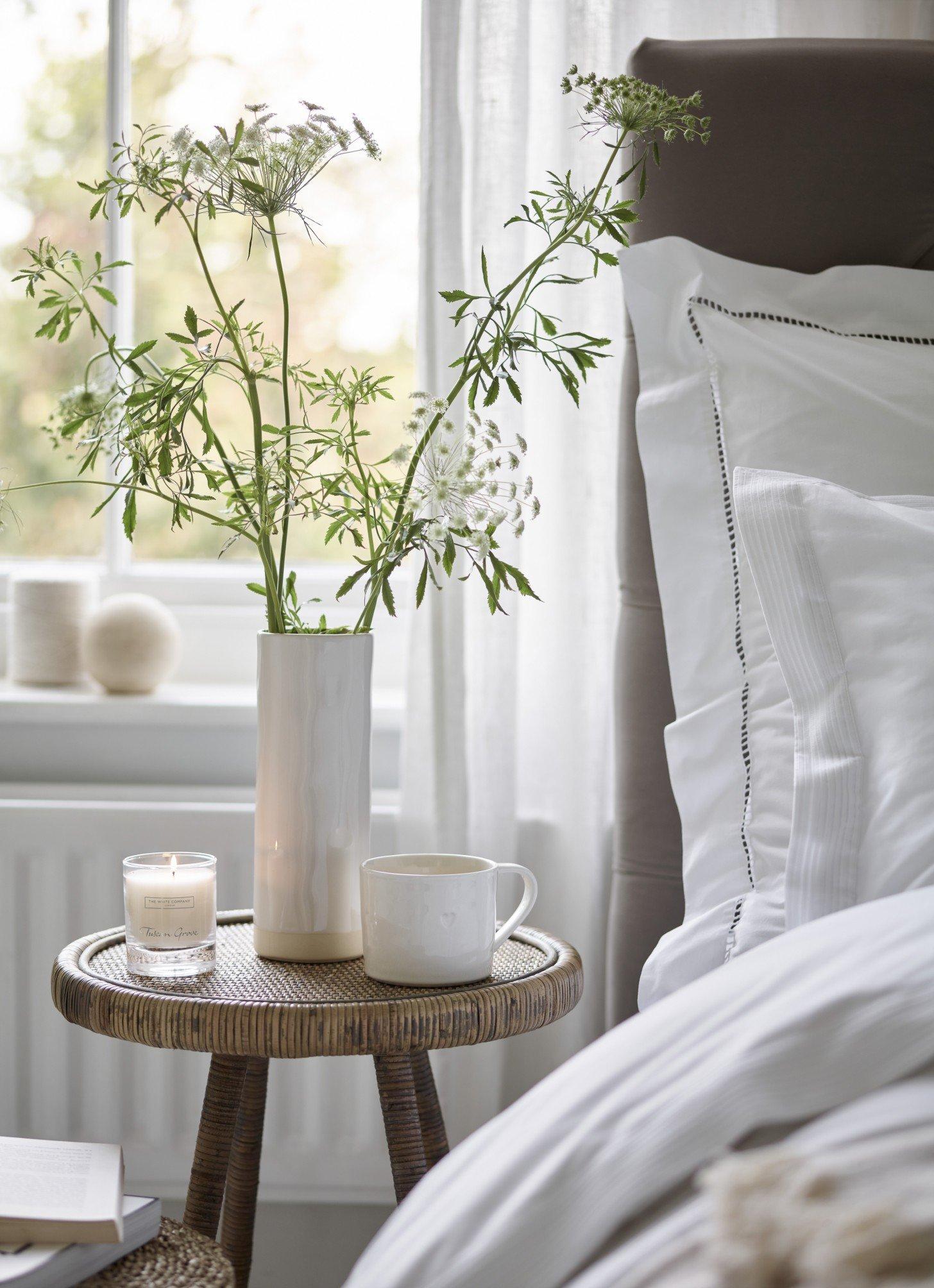 a bedside table with a vase of flowers and a cup of coffee