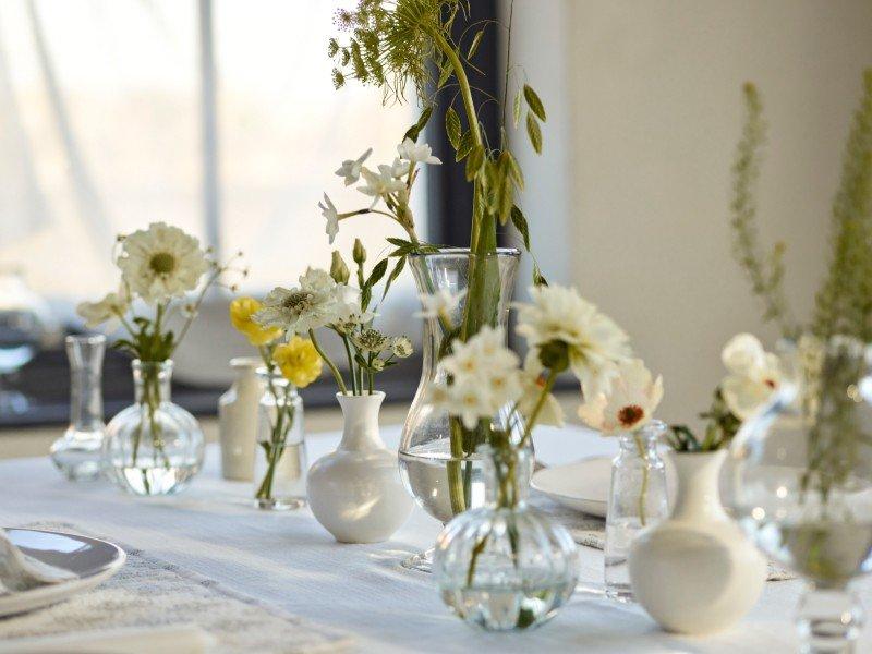 a table with white table cloth and white vases with flowers