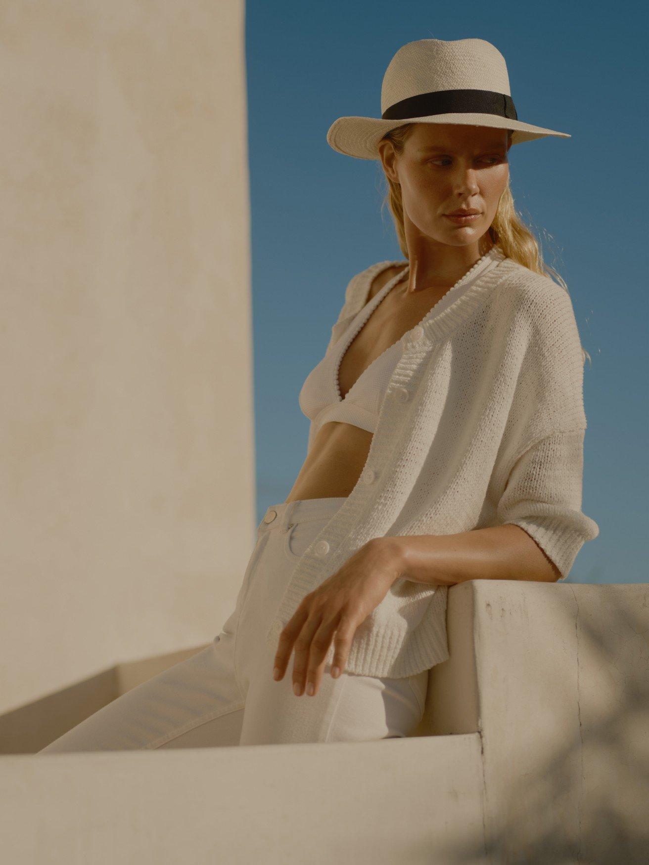 a woman in white hat and white pants leaning against a wall