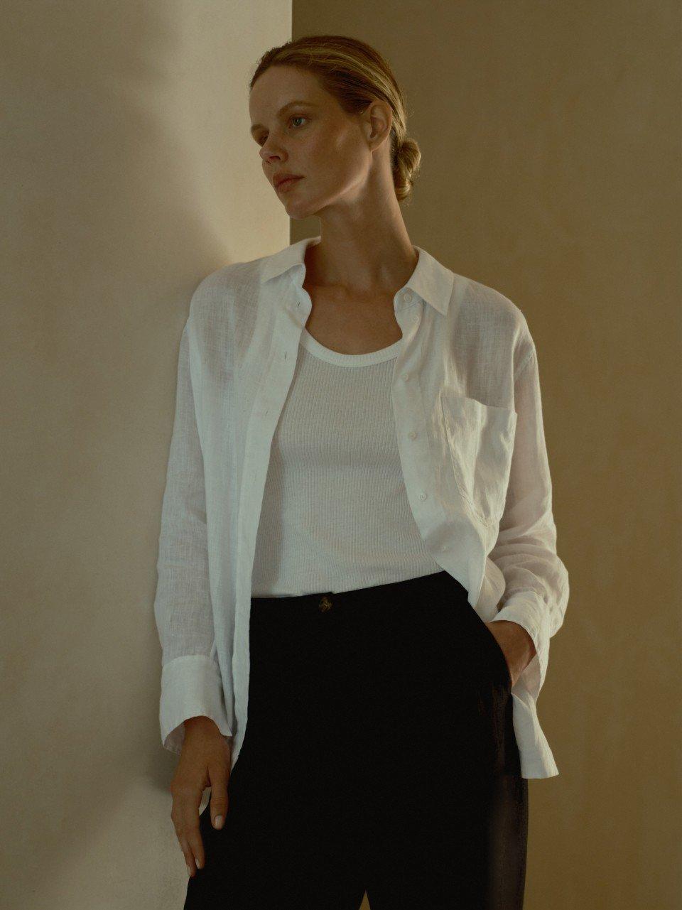 a woman in a white shirt and black pants leaning against a wall