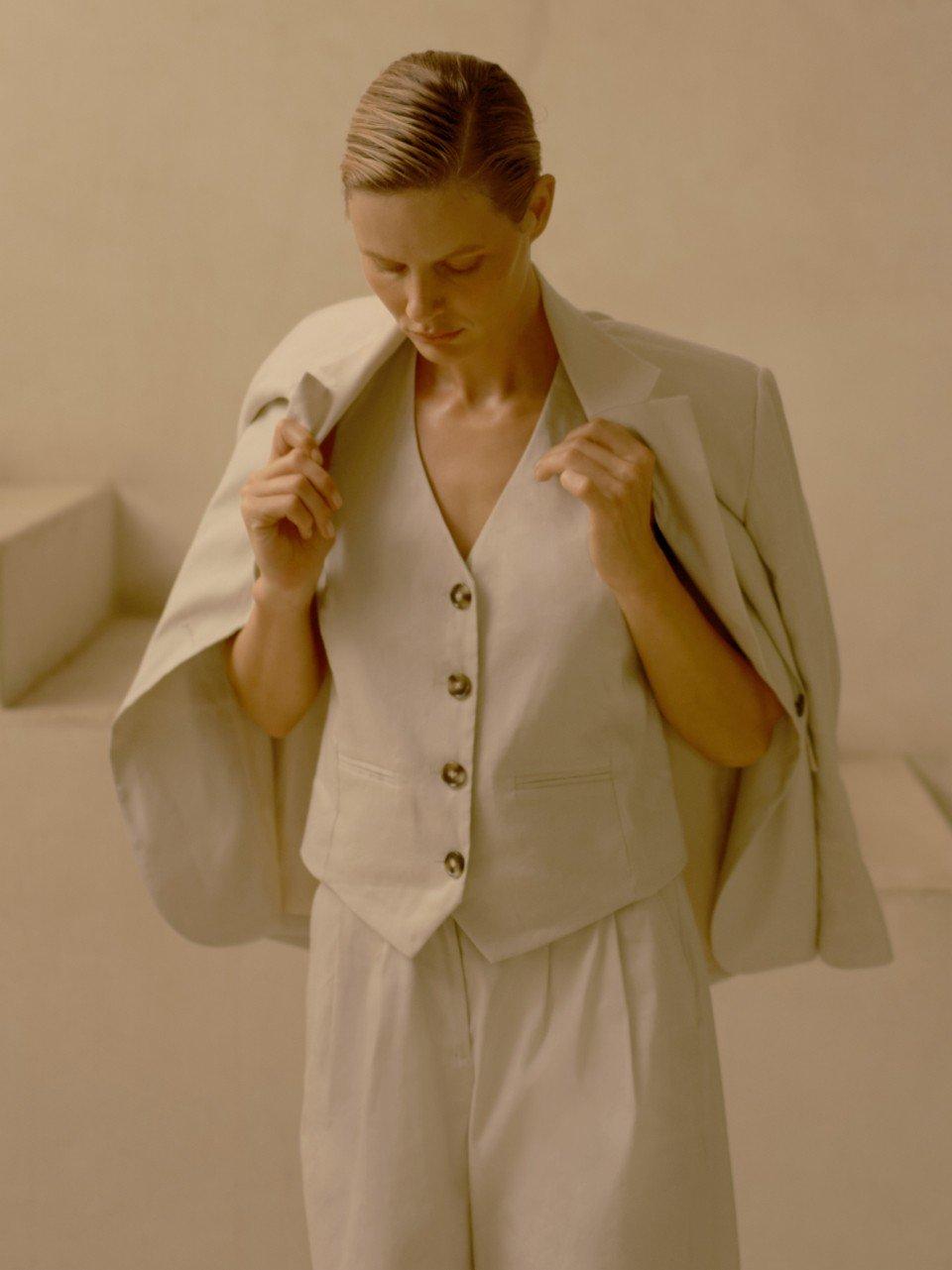 a woman in a white suit adjusting her jacket while standing