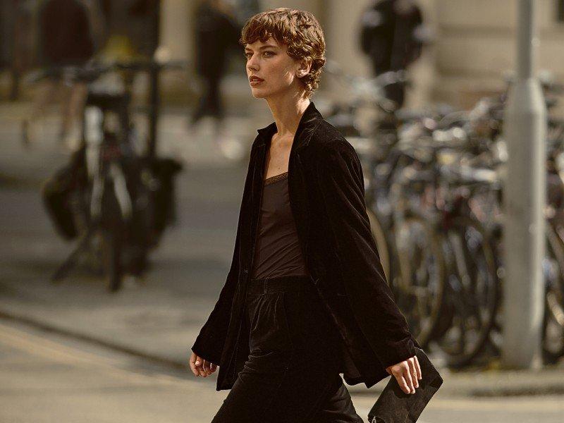 a woman in a black dress standing on a street corner