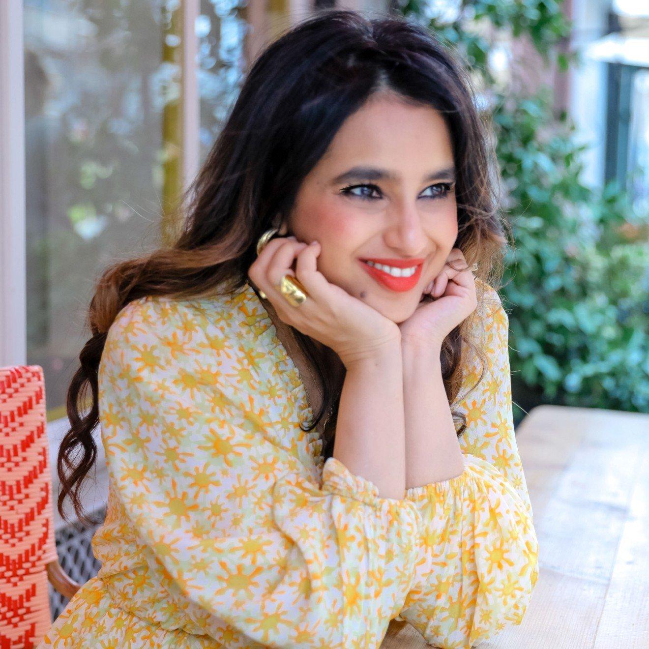 a woman in yellow dress sitting at a table with her hand on her chin