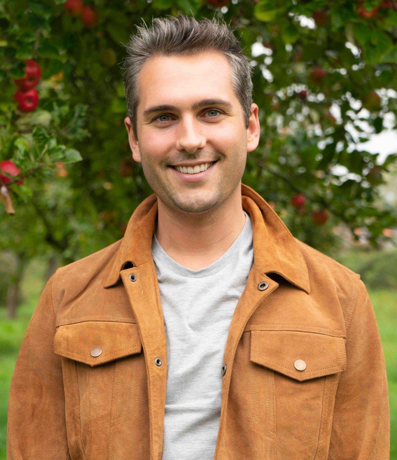 a man in a brown jacket smiling for the camera