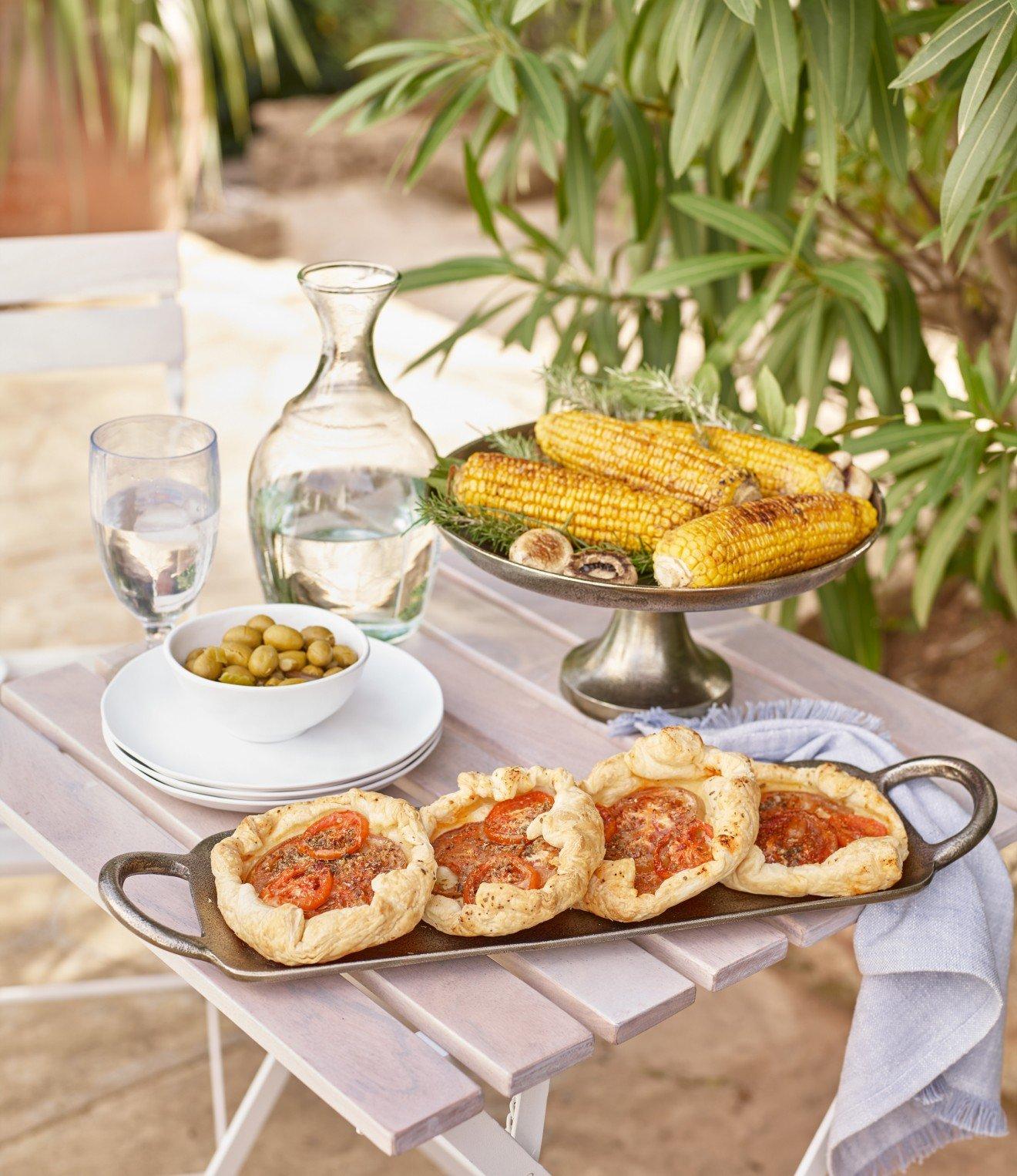 a table with a variety of food on it, including corn and tomatoes