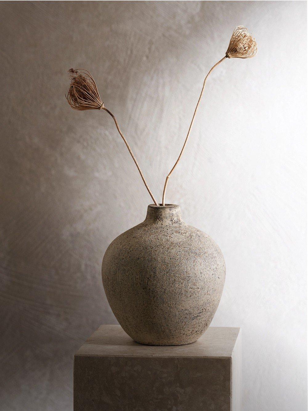 a vase with two dried flowers in it on a pedestal