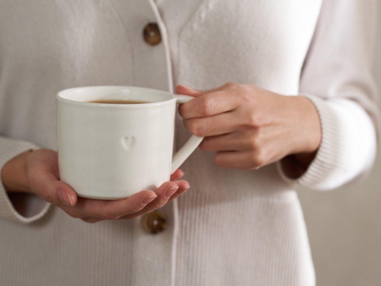 a woman holding a white mug with a heart on it