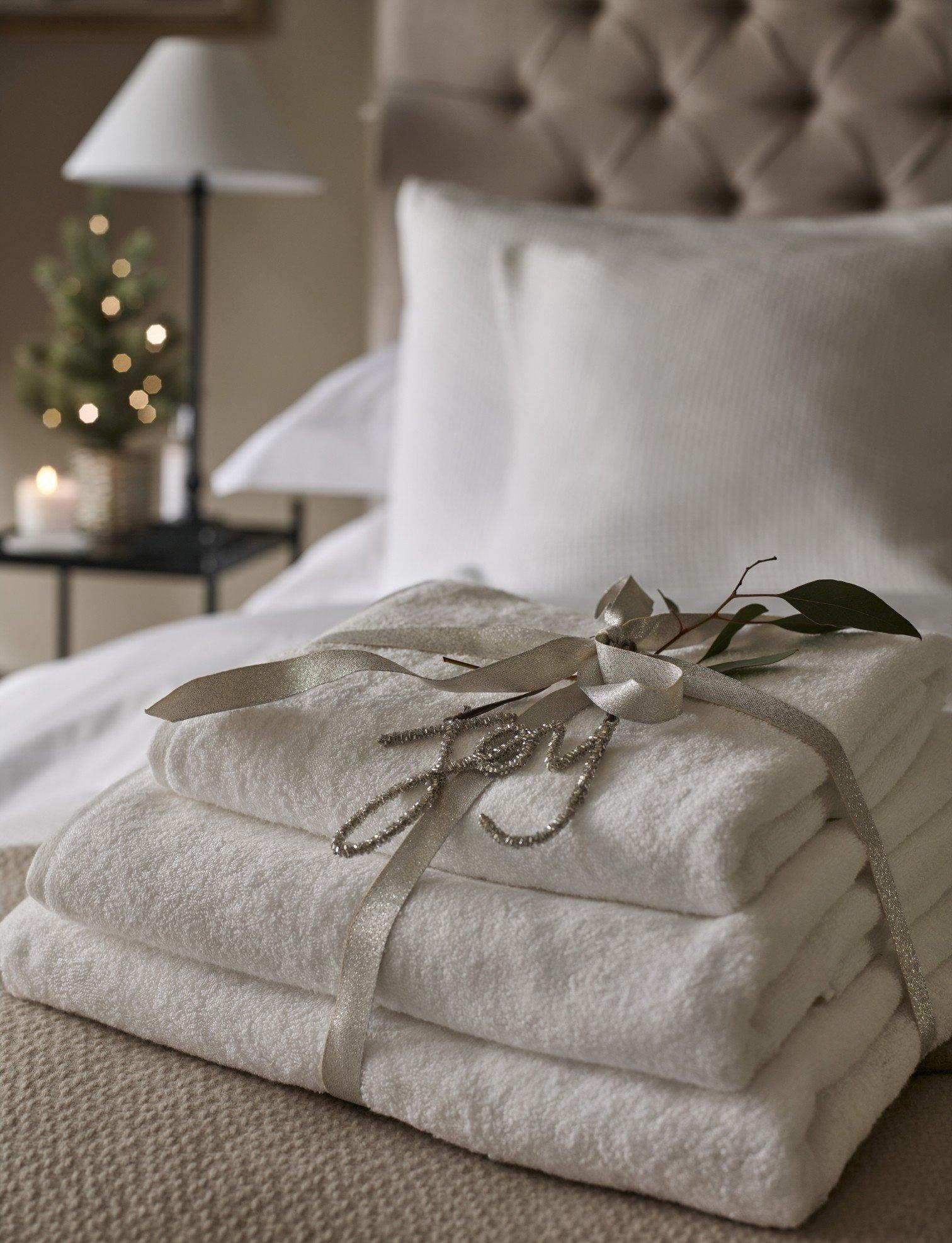 a stack of white towels on a bed with a white lamp
