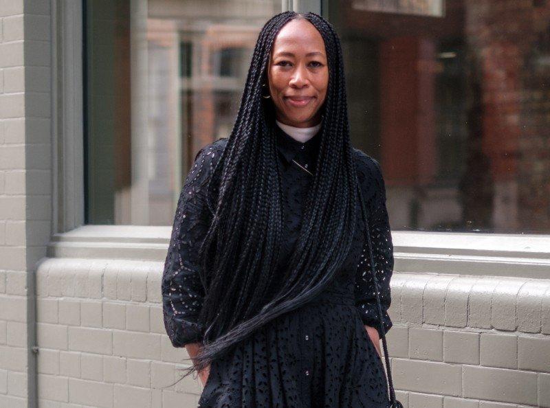 a woman with long braids standing on a sidewalk with a purse