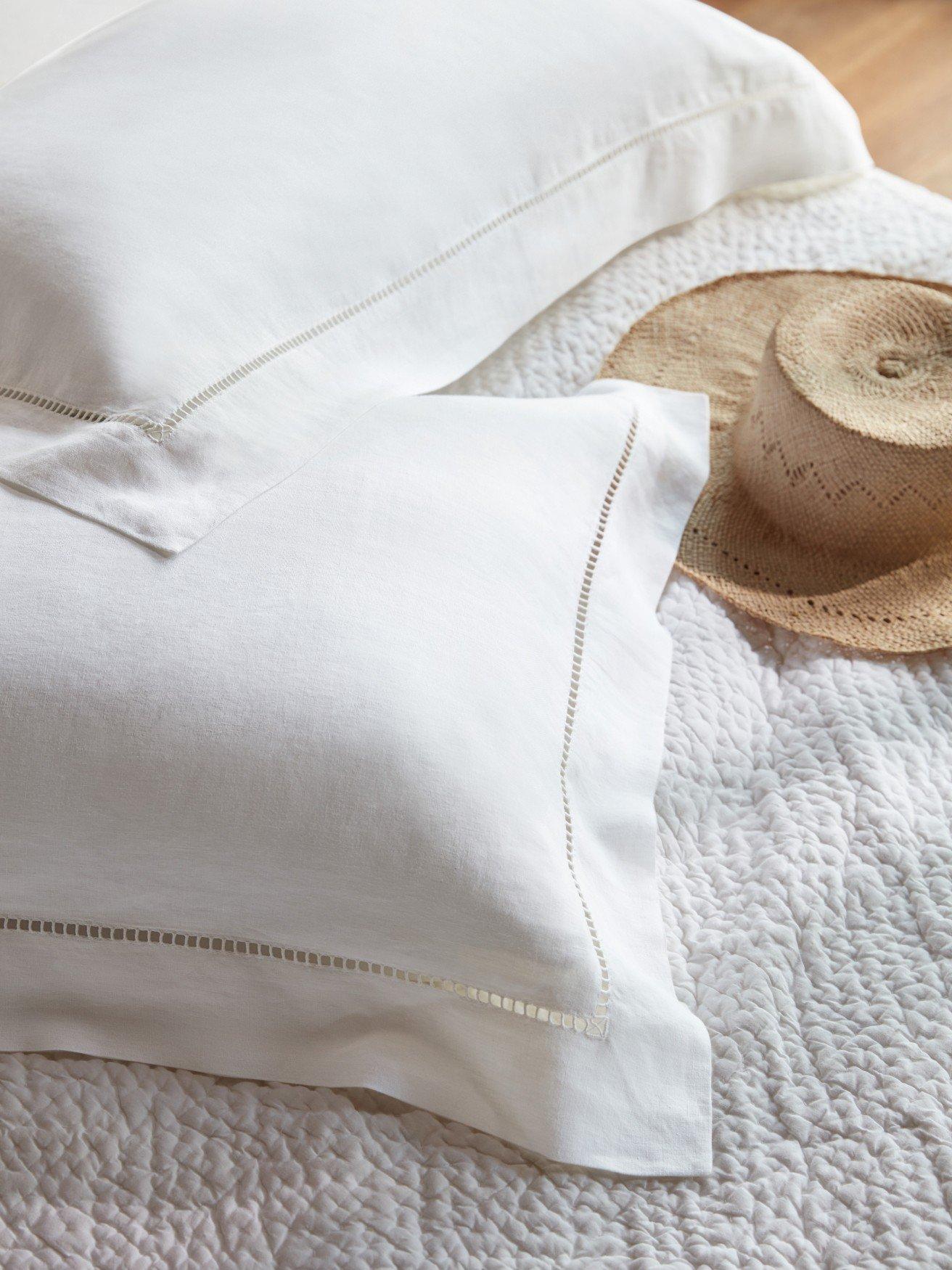 a bed with white sheets and a straw hat on top