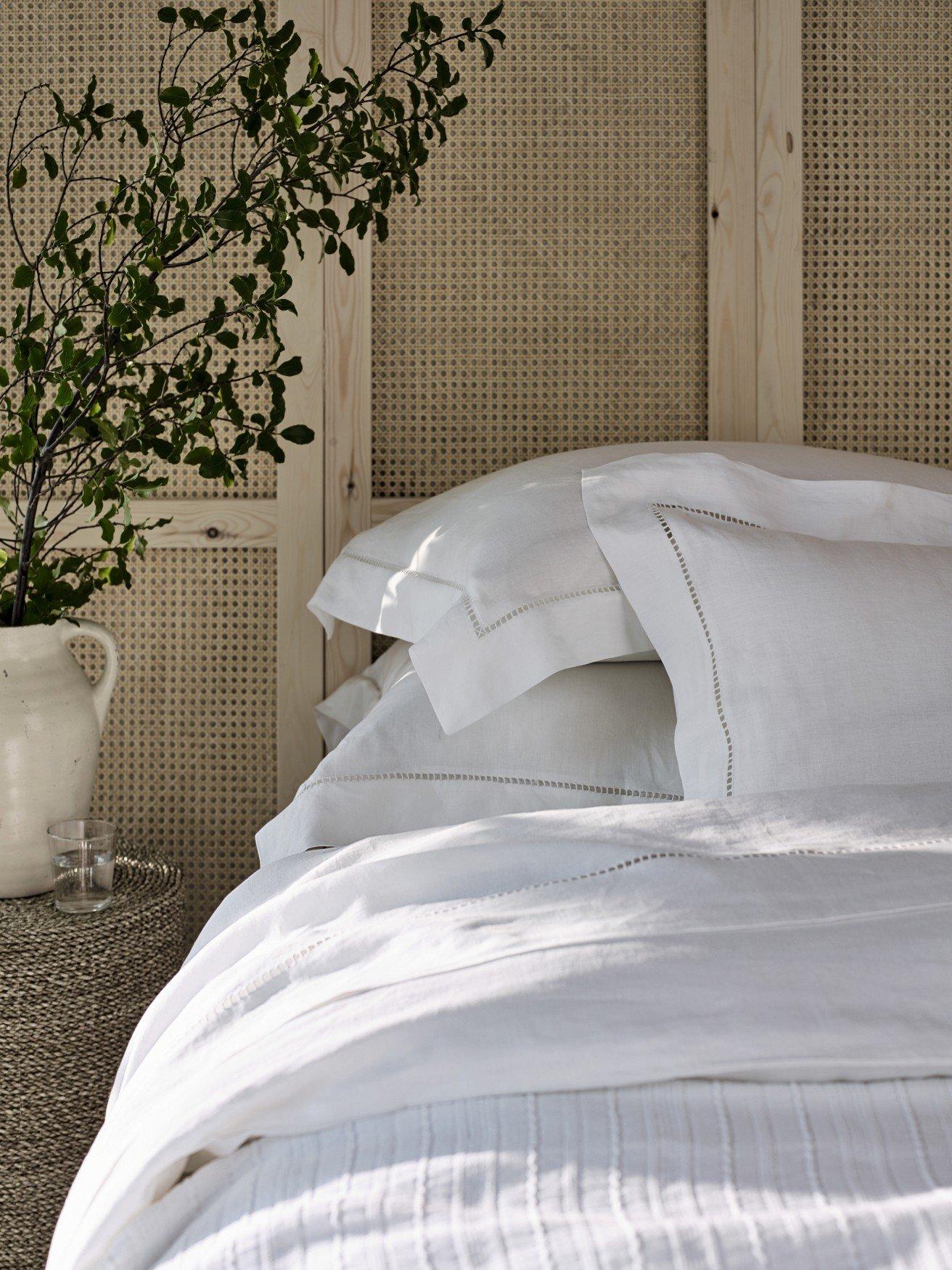 a bed with white sheets and pillows and a vase of flowers