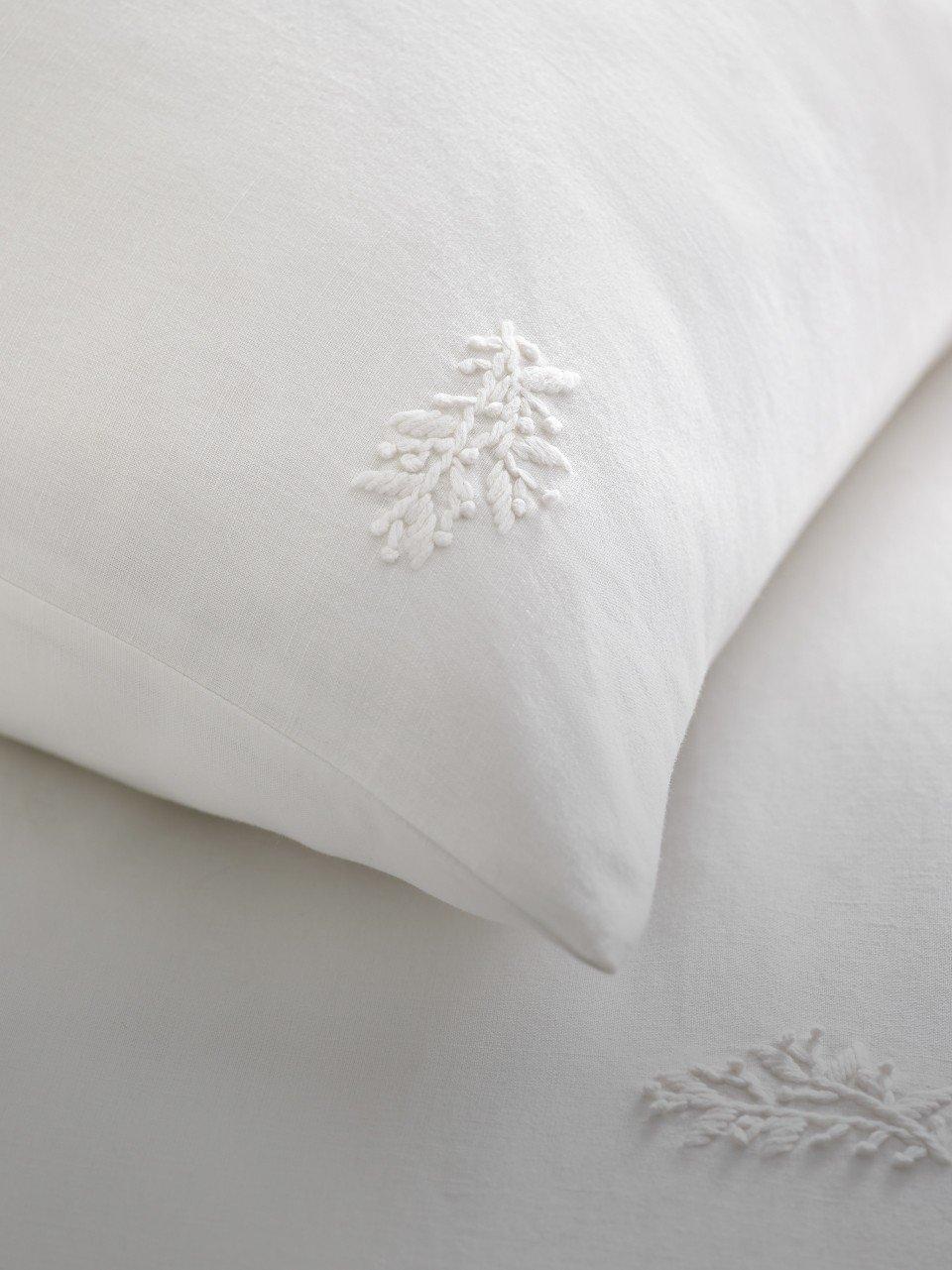 a close up of a white pillow with embroidered leaves on it