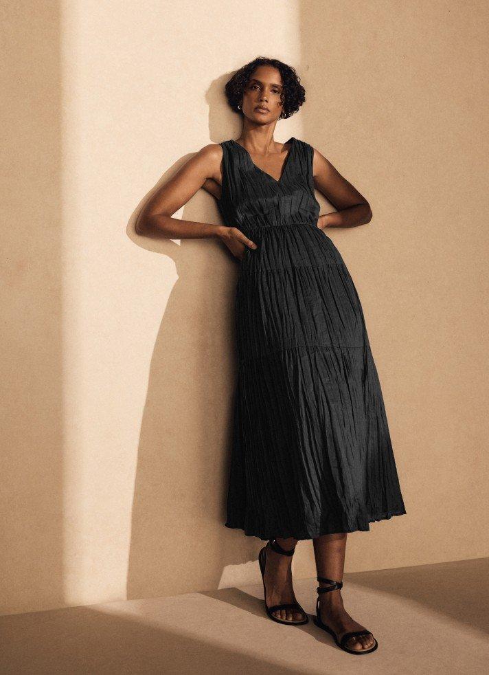 a woman in a black dress leaning against a wall