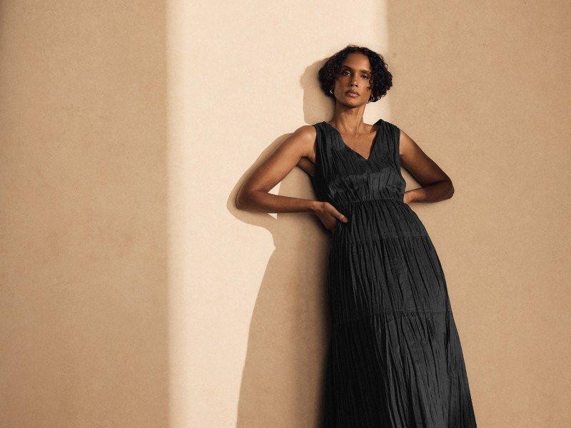a woman in a black dress leaning against a wall