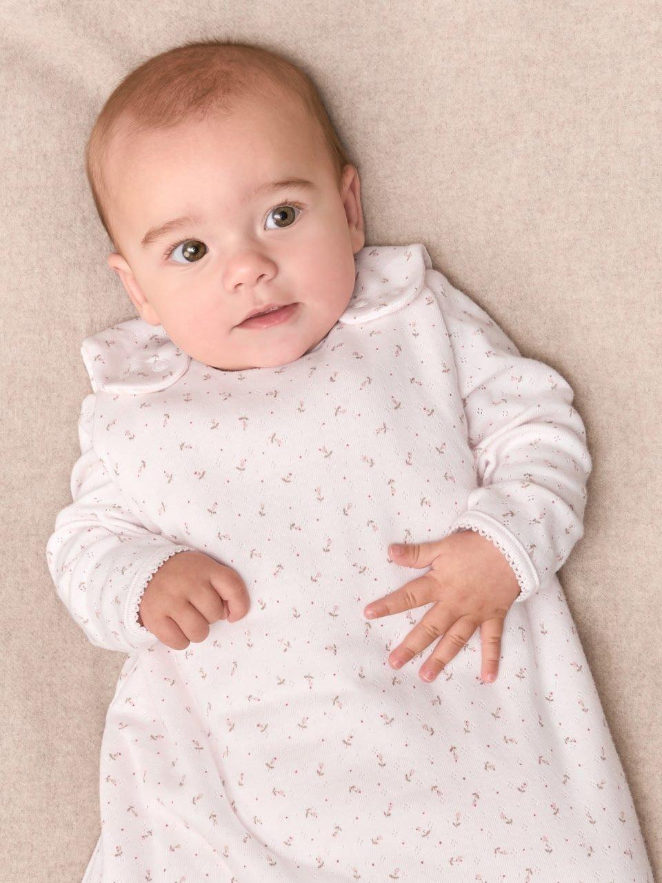 a baby laying on a bed wearing a white sleeper