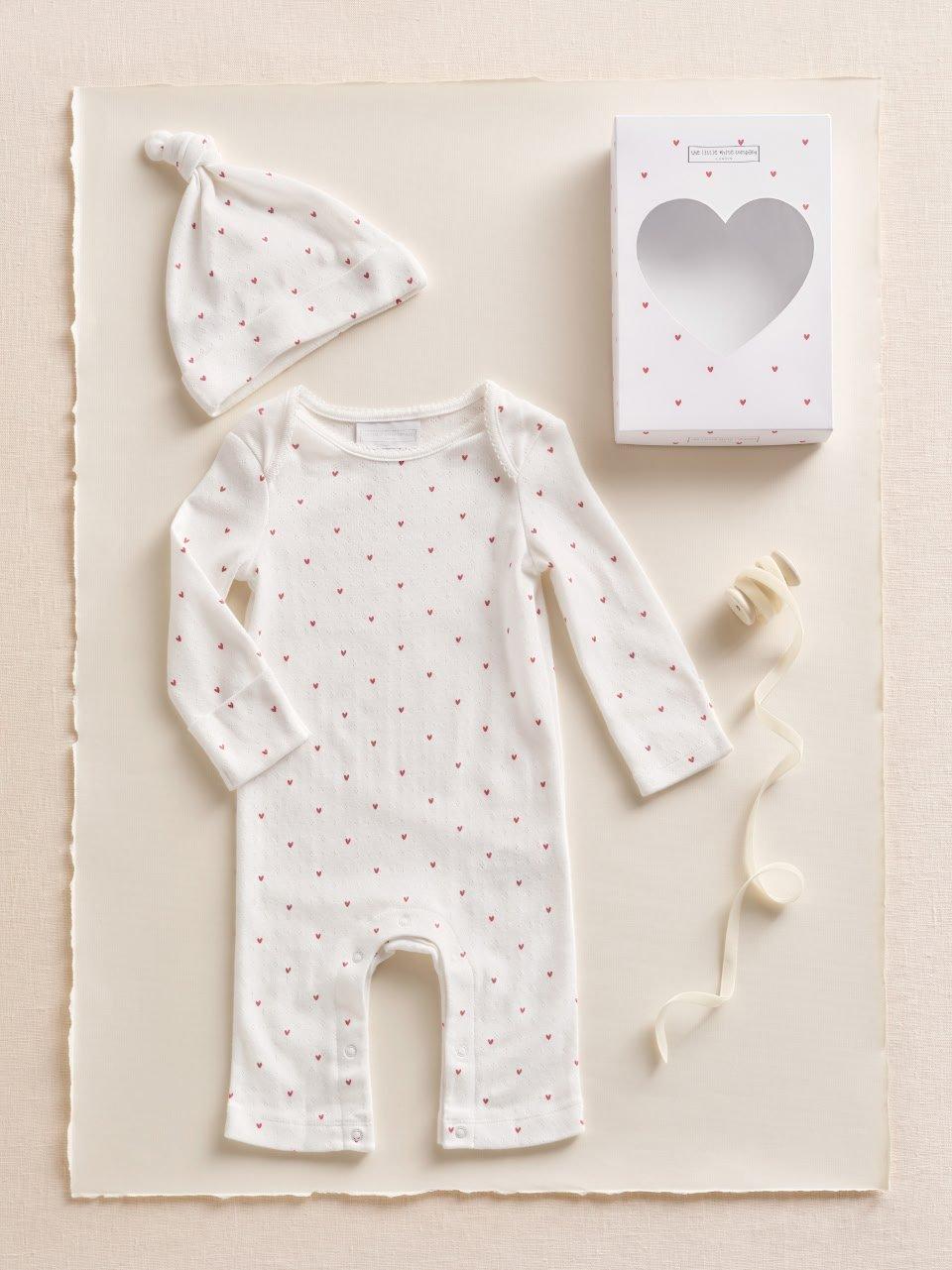 a baby's white romper with a heart print and a hat