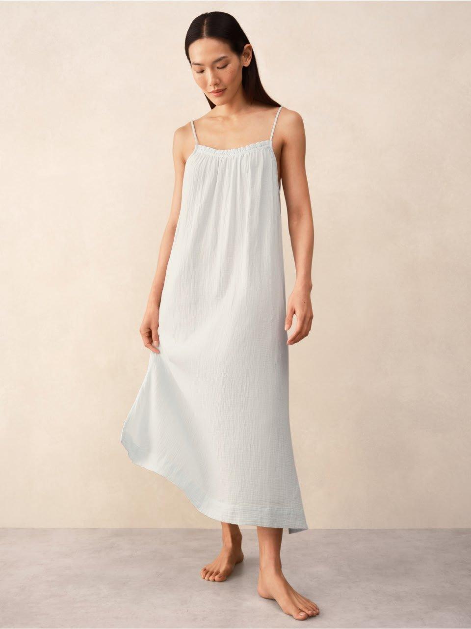 a woman in a white slip dress stands on a white floor