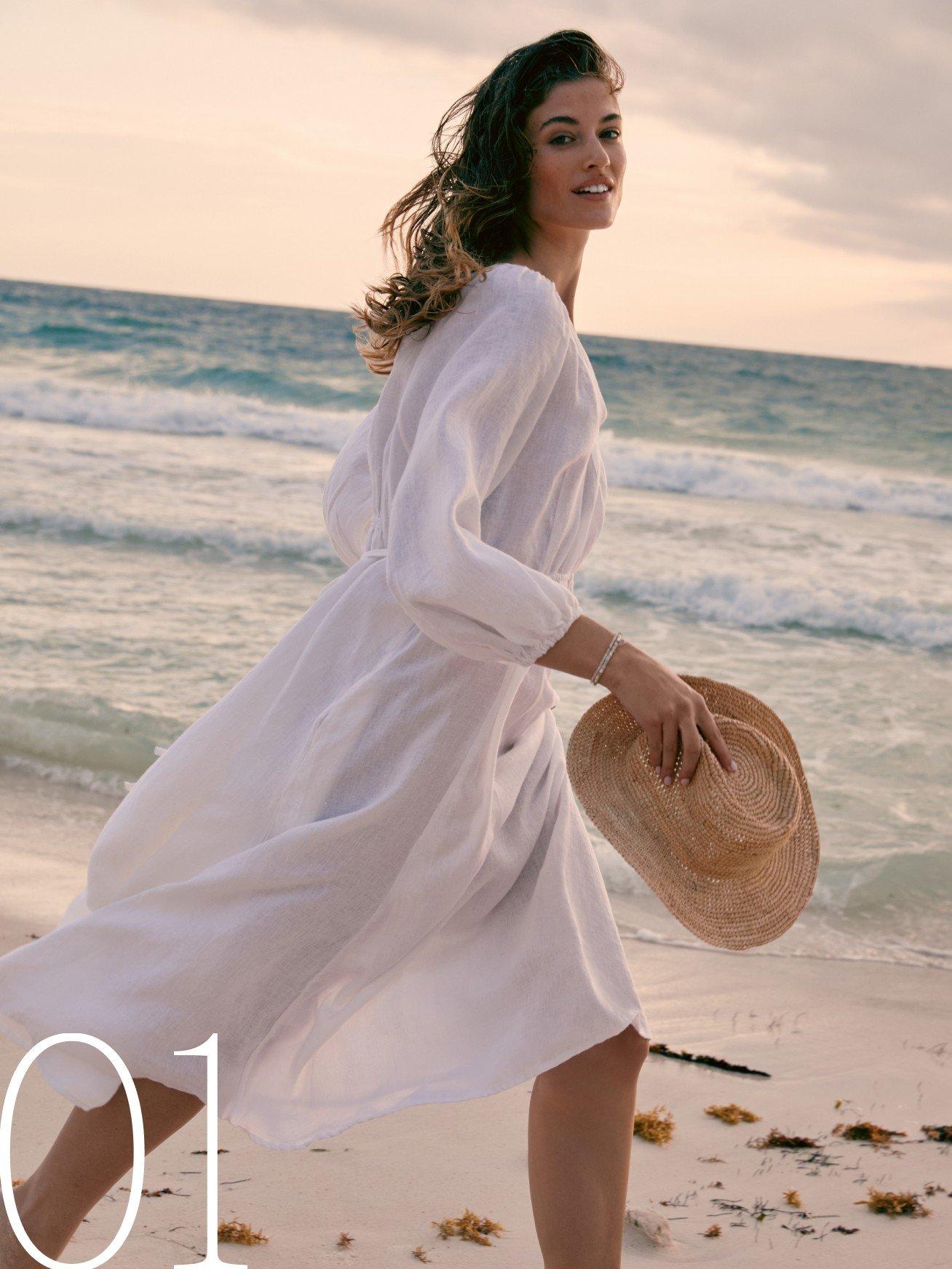 a woman in a white dress walking on the beach