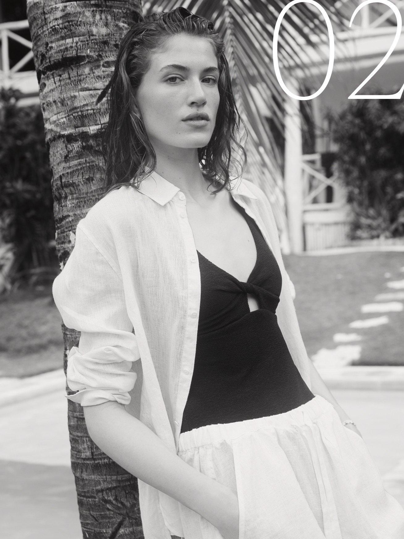 a woman in a white shirt and black shorts leaning against a tree