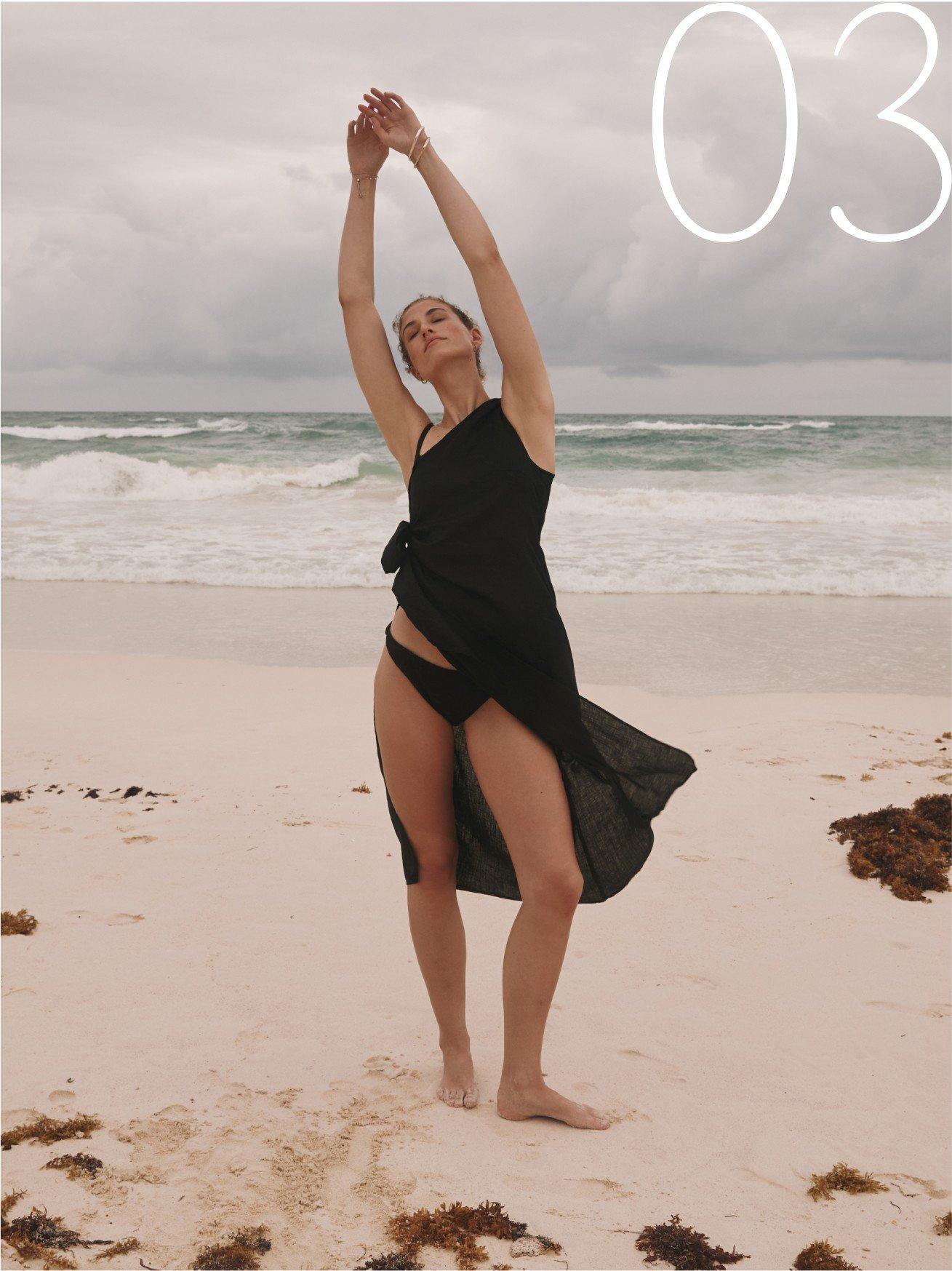 a woman in a black dress standing on a beach with a frisbee
