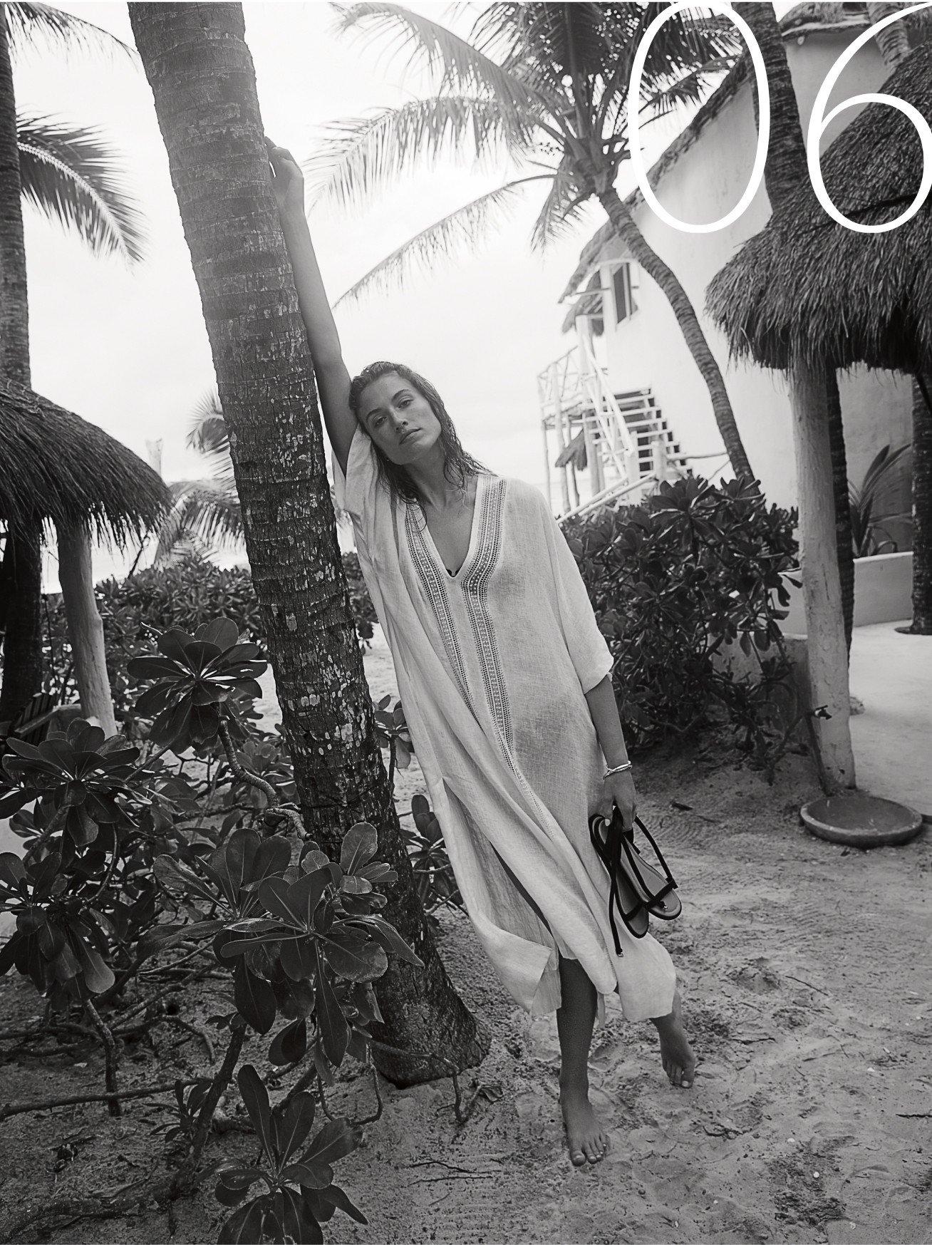 a woman in a white dress leaning on a palm tree