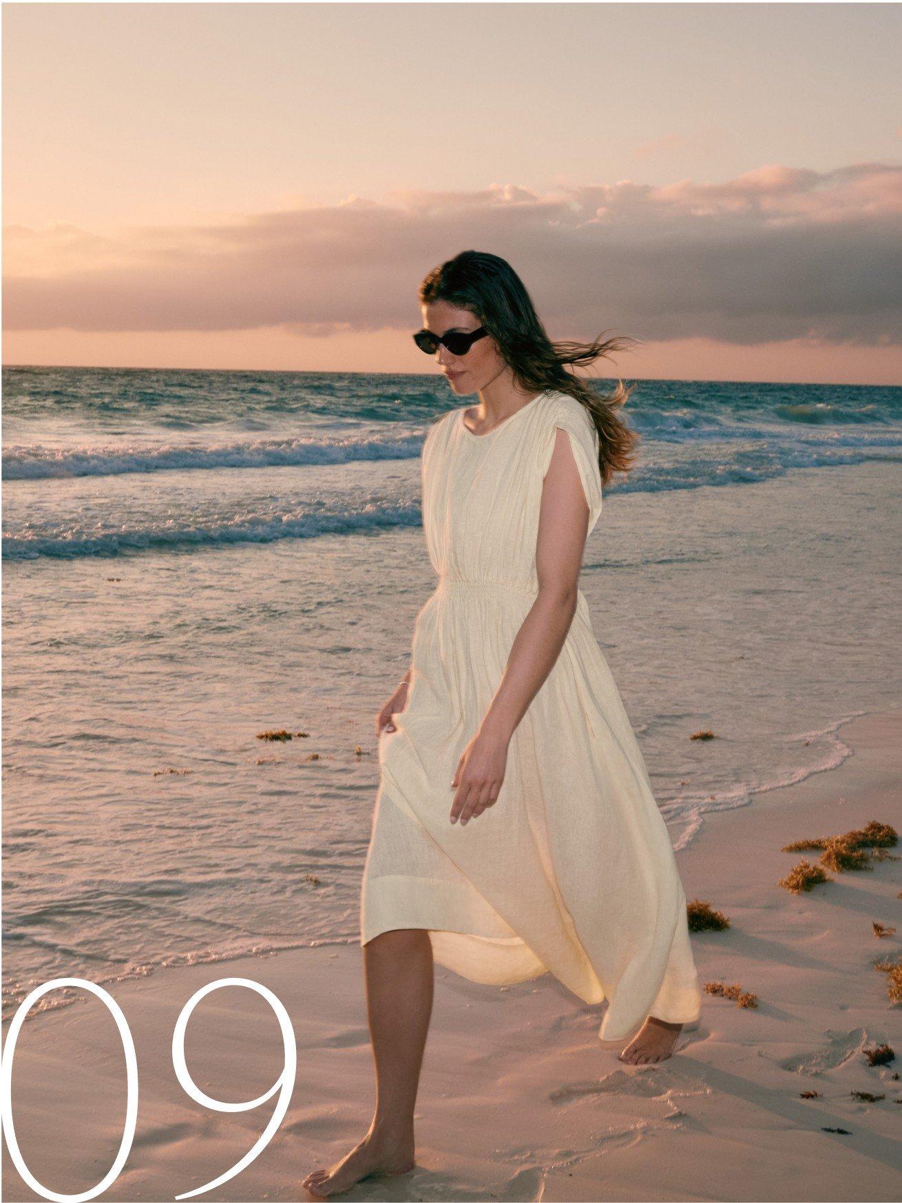a woman walking on the beach in a white dress