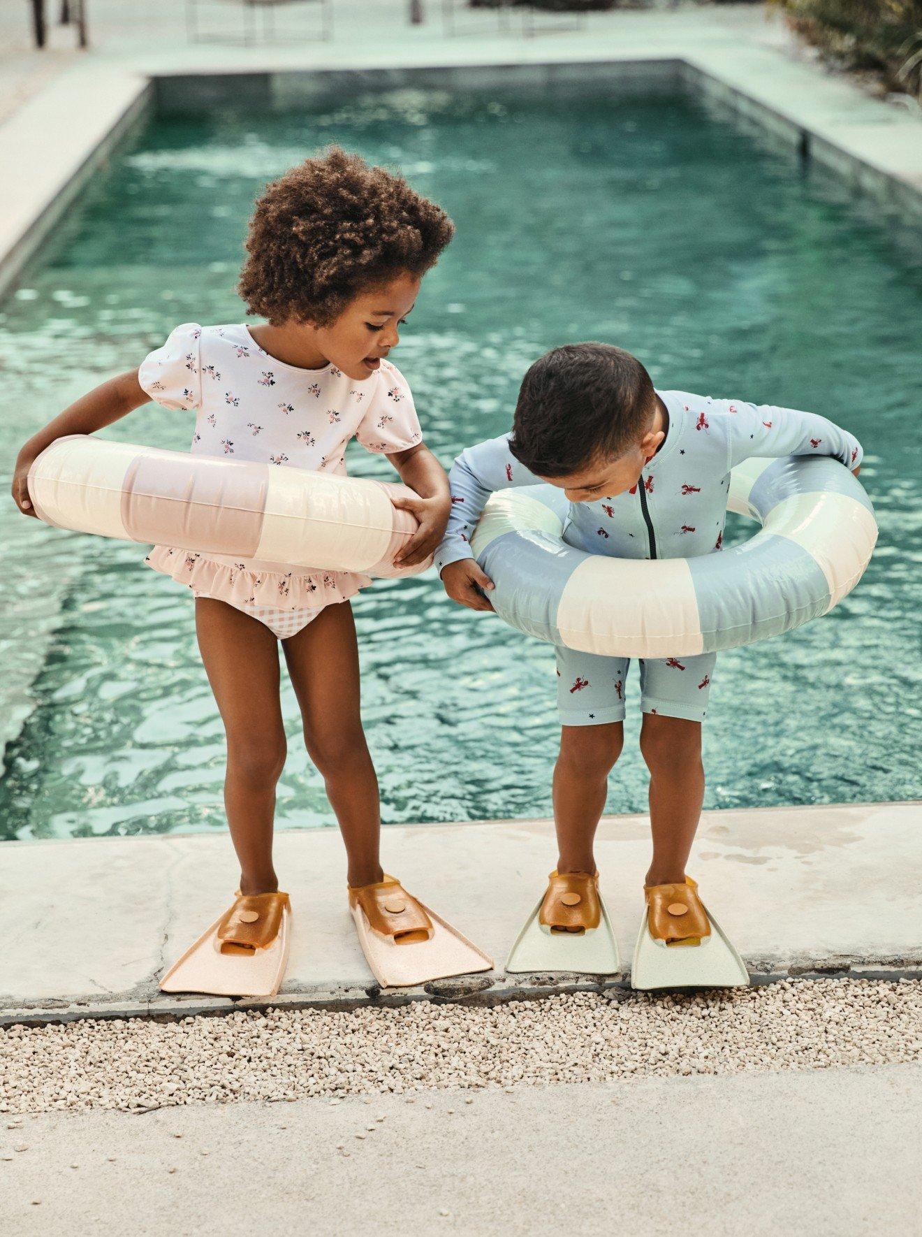 two children standing by a pool with flippers and rings