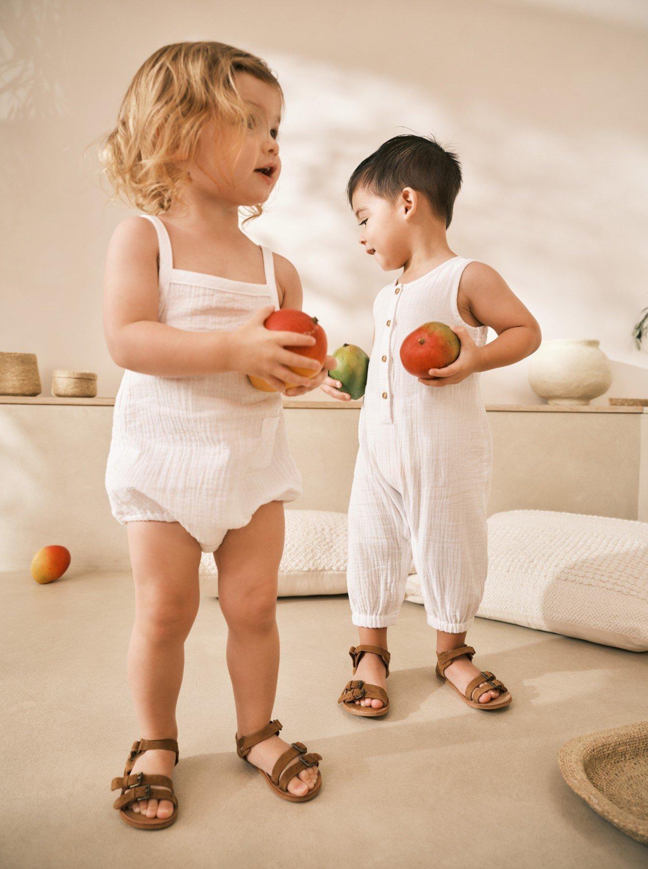 two children in white outfits holding apples in their hands