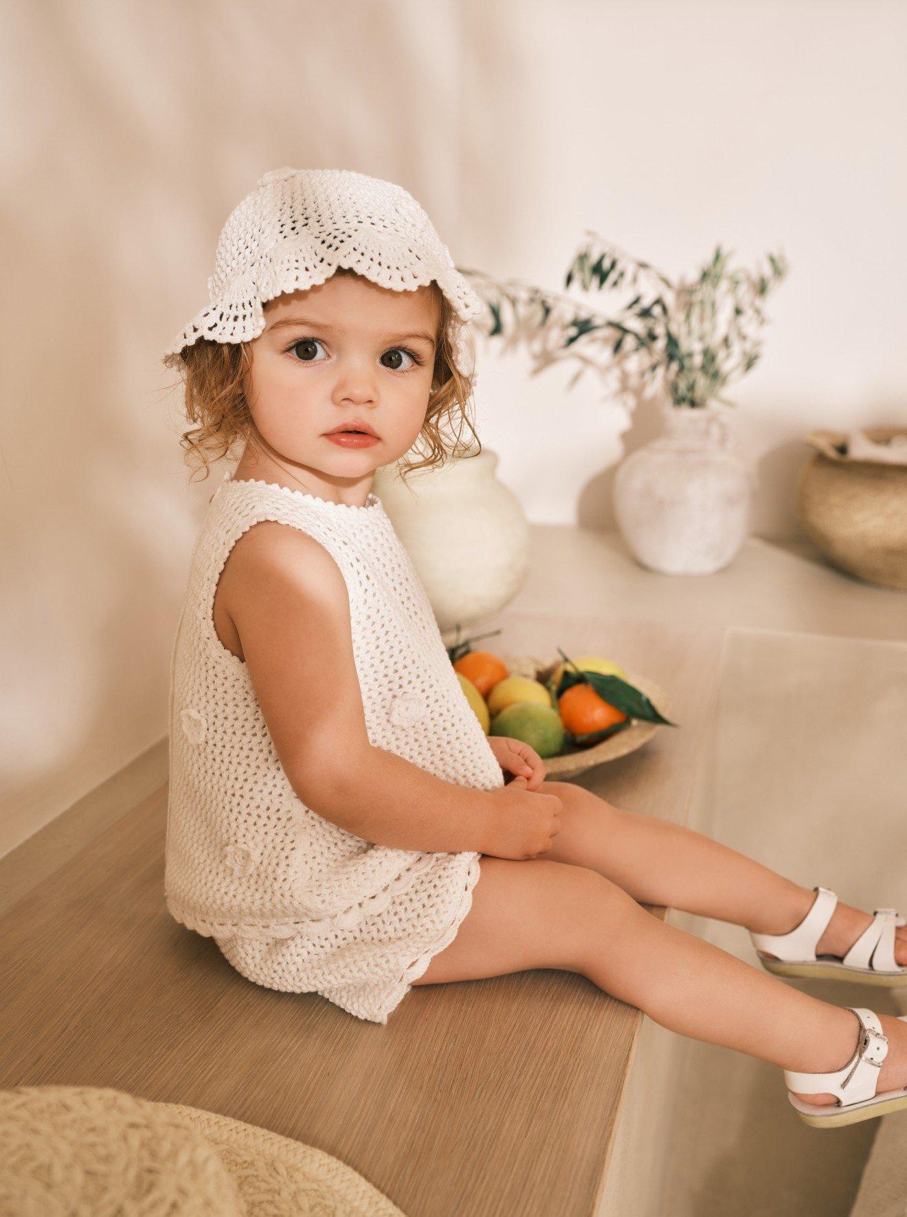 a little girl sitting on a ledge with a bowl of fruit