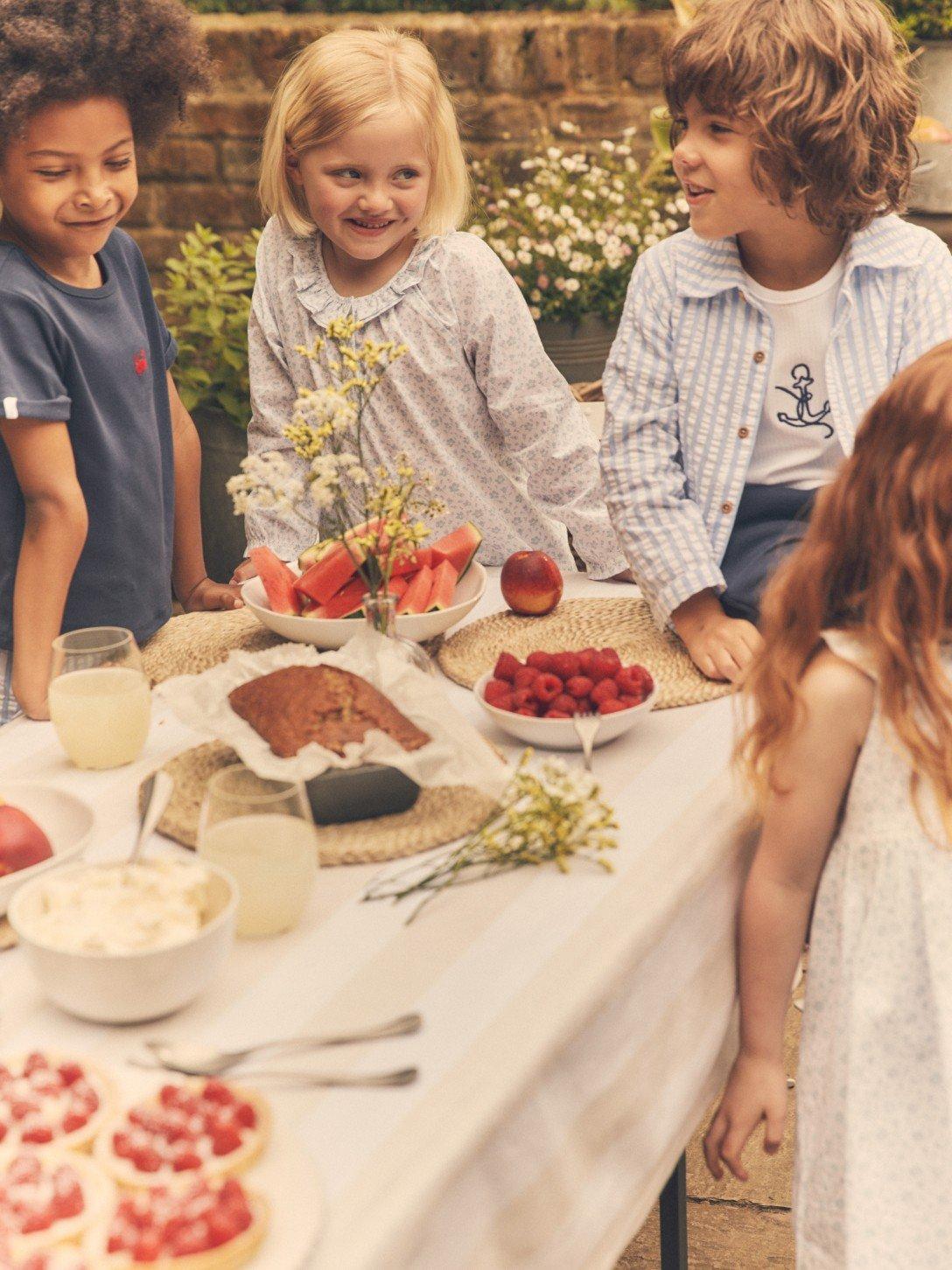 a group of children are gathered around a table with food