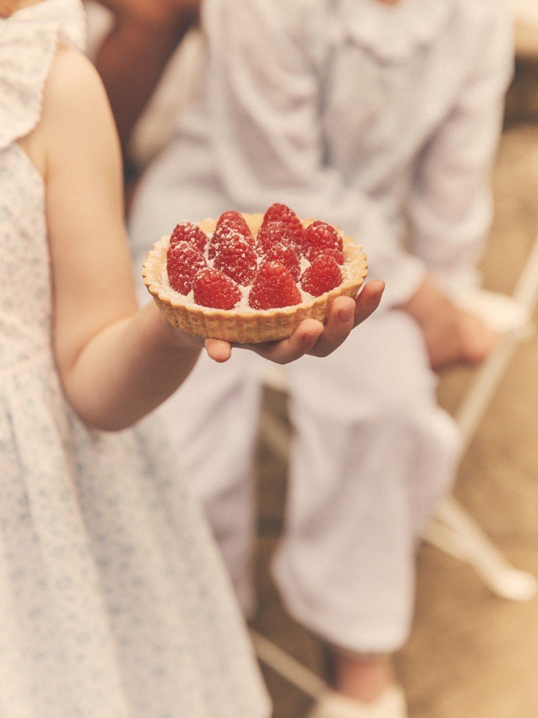 a person holding a small dish of raspberries in a white dress