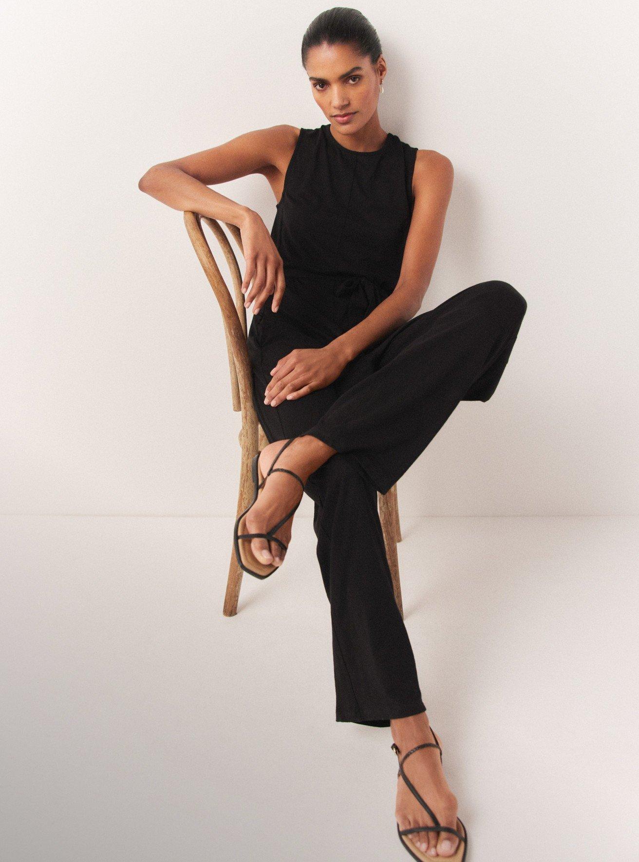 a woman in black sitting on a chair wearing sandals