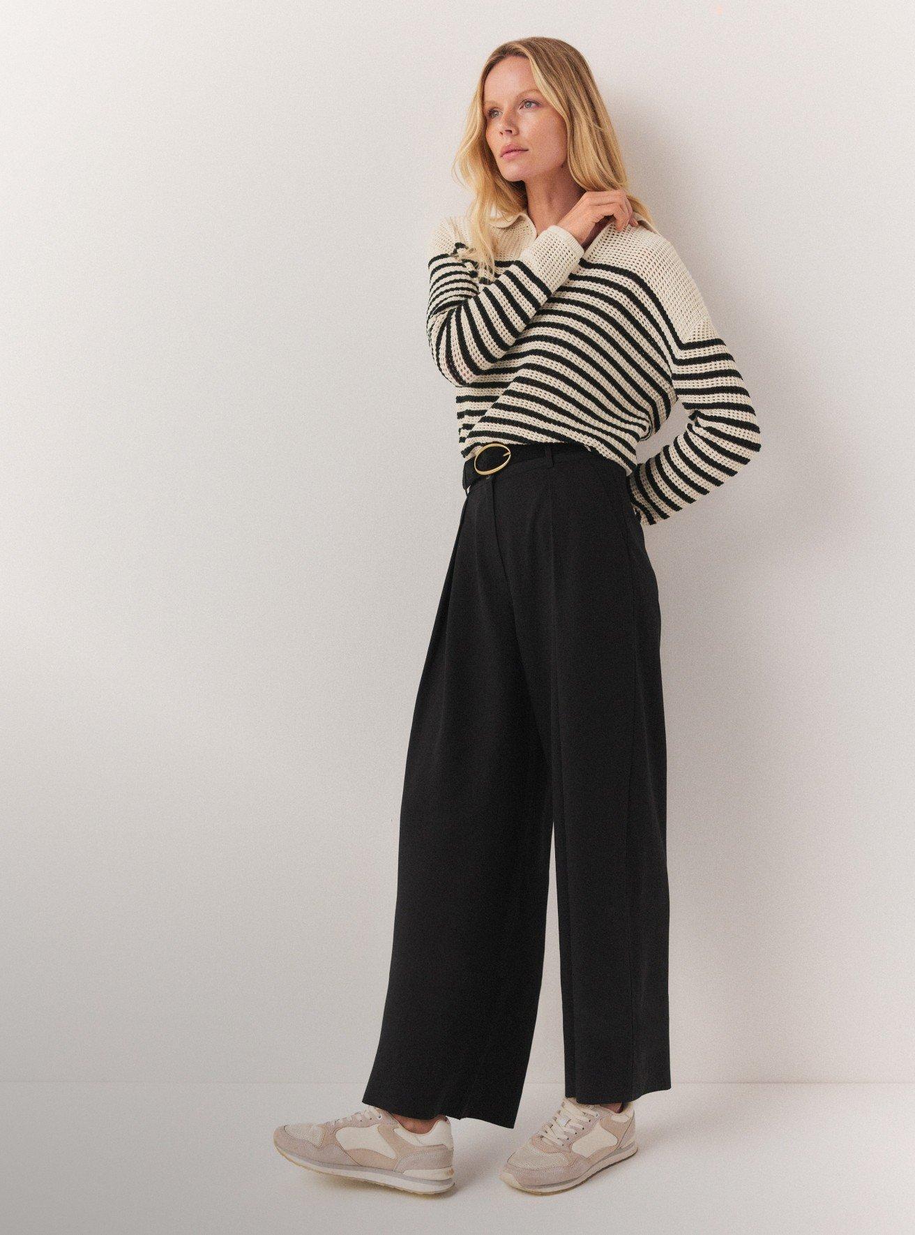 woman in striped sweater and wide leg pants standing against wall