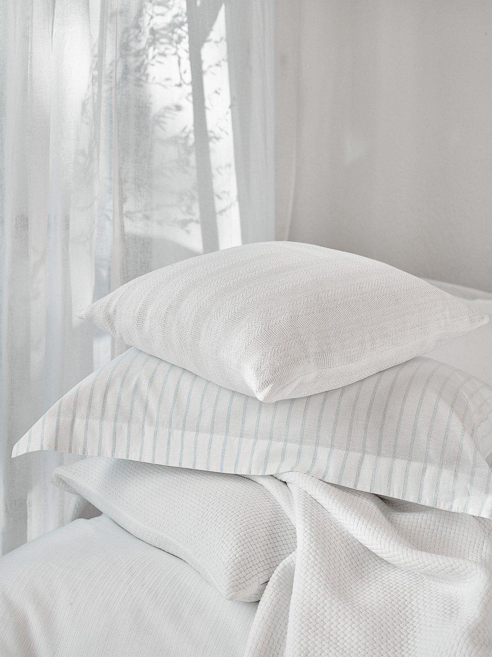 a pile of pillows on a bed with a window behind them