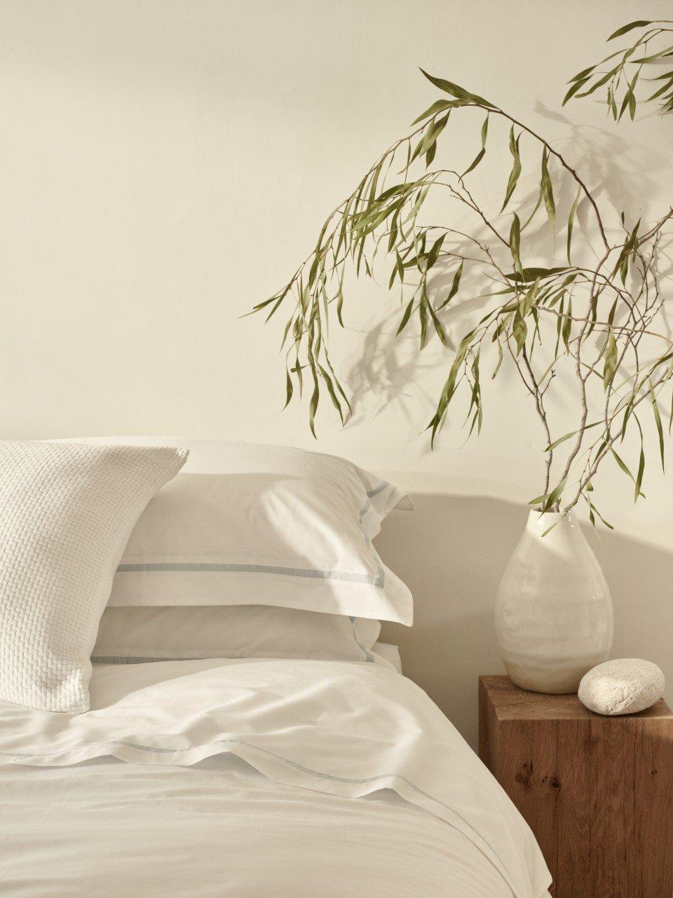 a white bed with white sheets and pillows next to a wooden vase