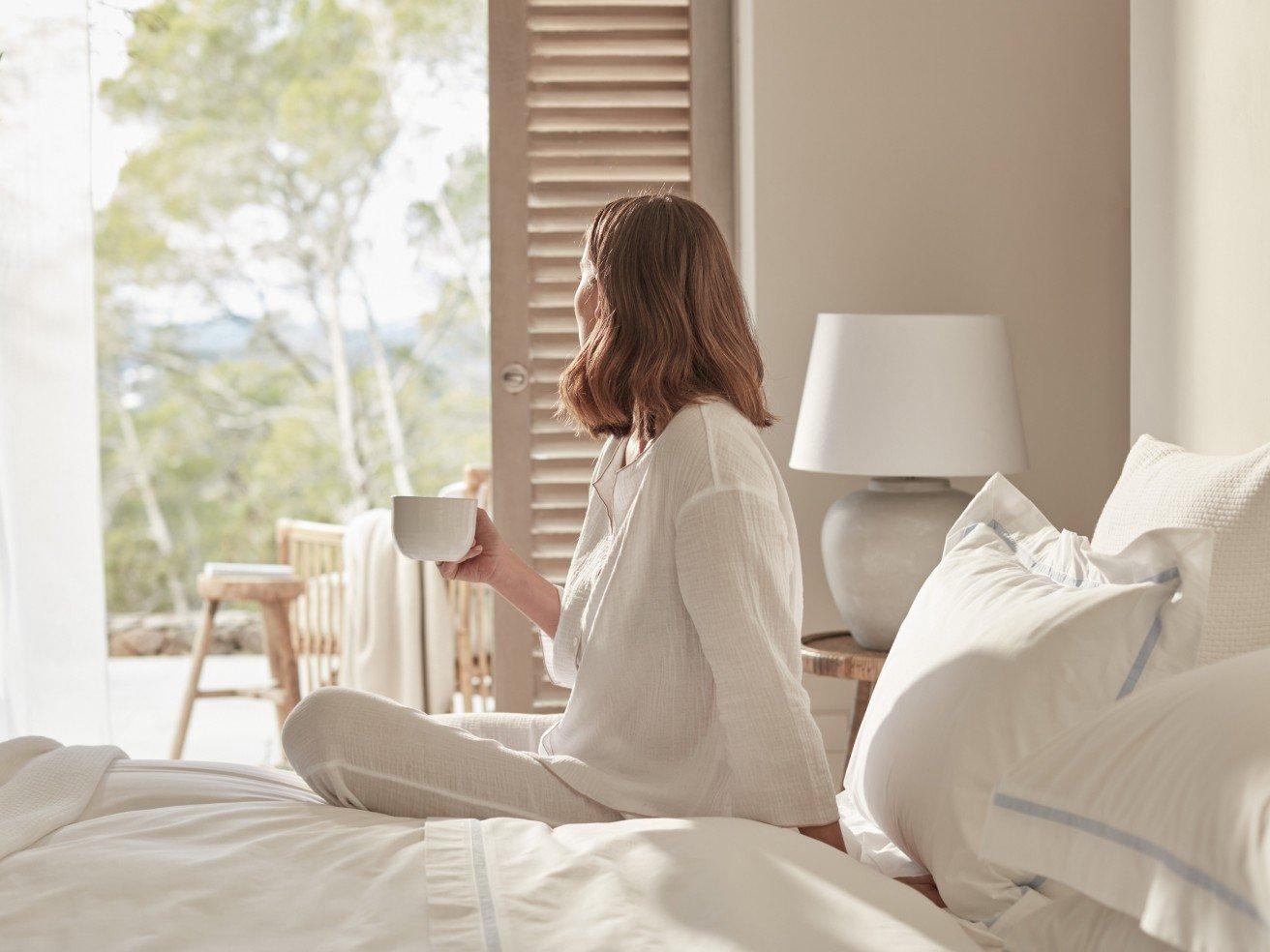 a woman in white pajamas sitting on a bed with a cup