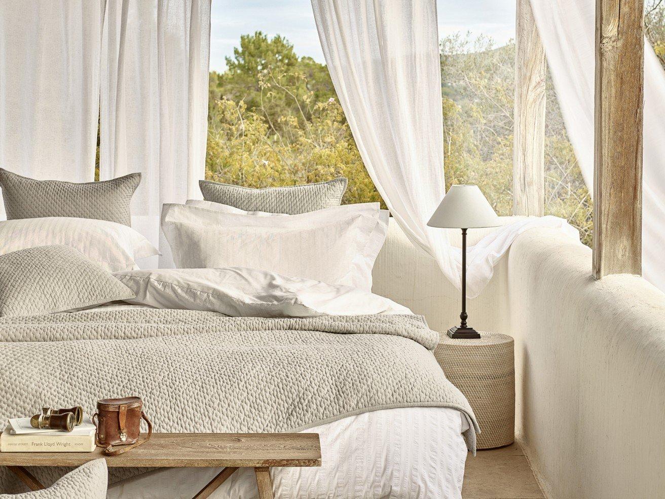 a bed with white sheets and pillows in a room with white curtains