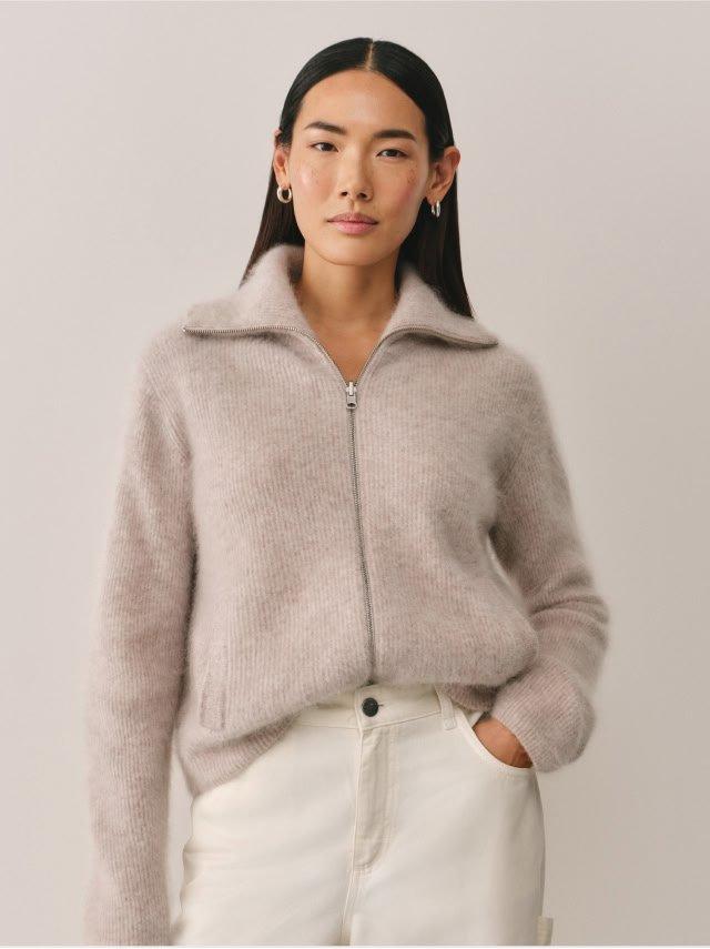 a woman in white pants and a grey sweater is posing for a picture