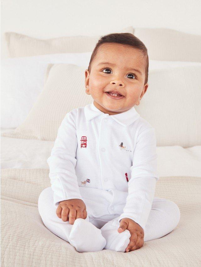 a baby is sitting on a bed wearing a white outfit