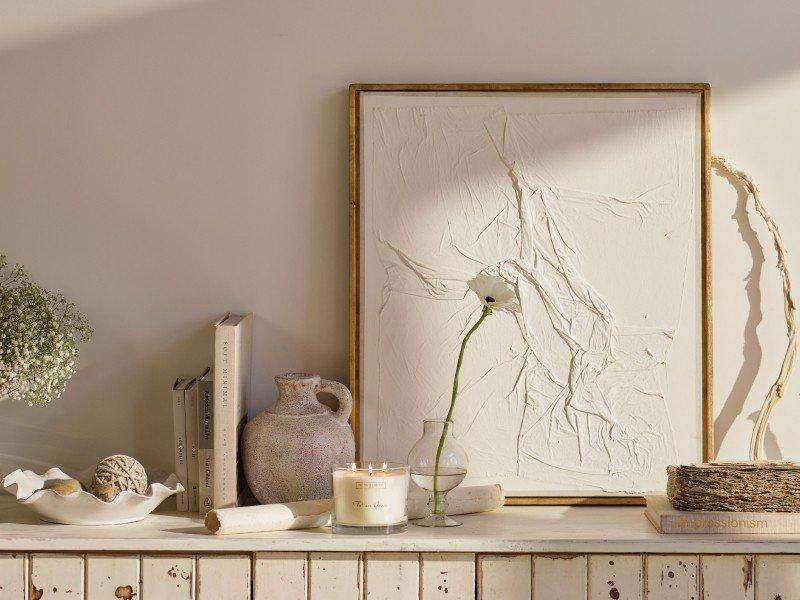 a white shelf with a candle, vase and flowers on it