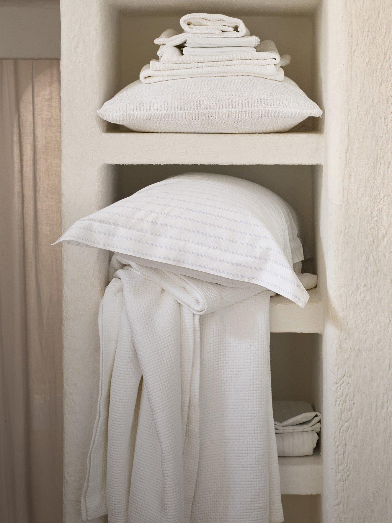 a shelf with a stack of white towels and pillows