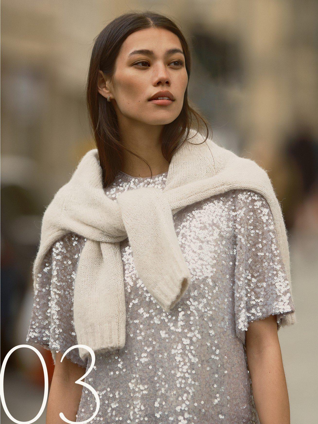 a woman in a sequined top and scarf walking down the street