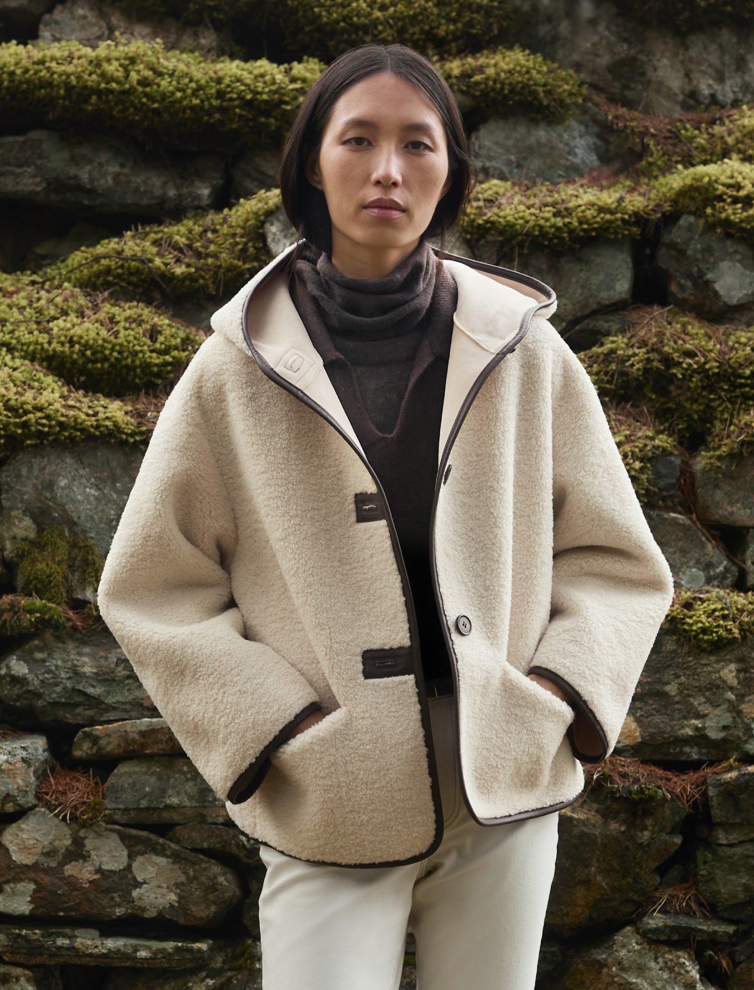 a woman in a white coat standing next to a stone wall