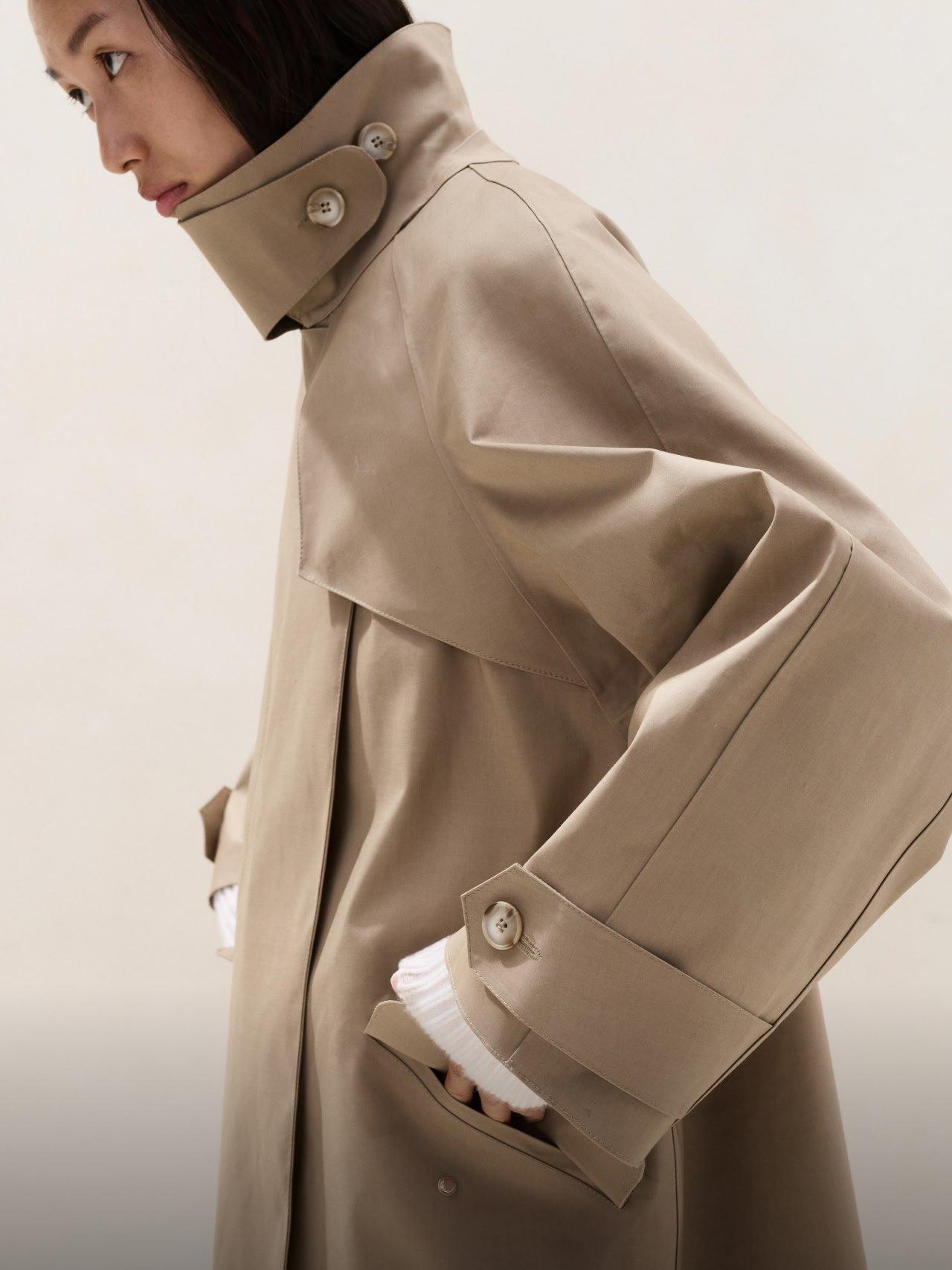 a woman in a trench coat standing with her hands in her pockets