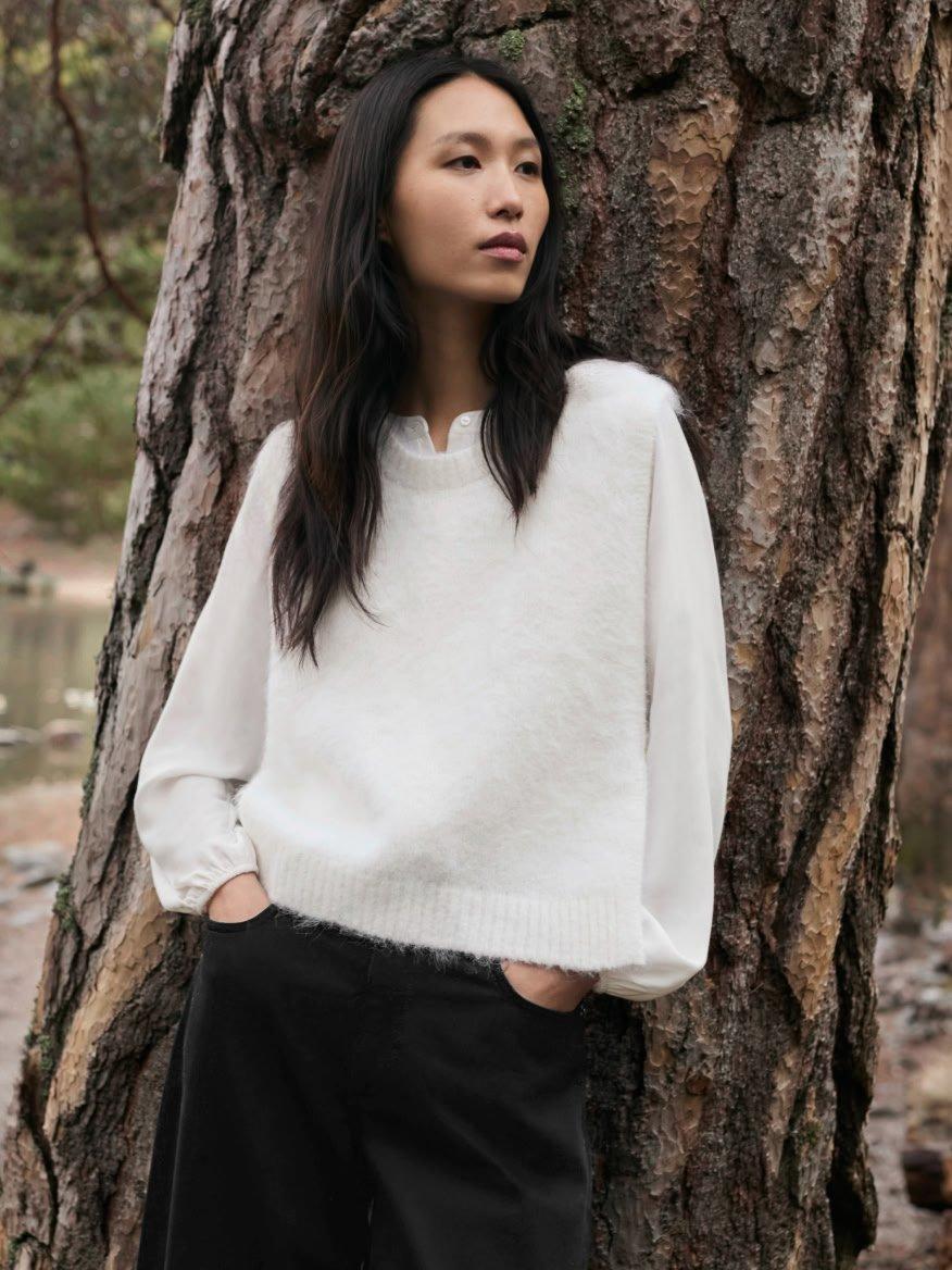 a woman standing next to a tree wearing black pants and a white sweater
