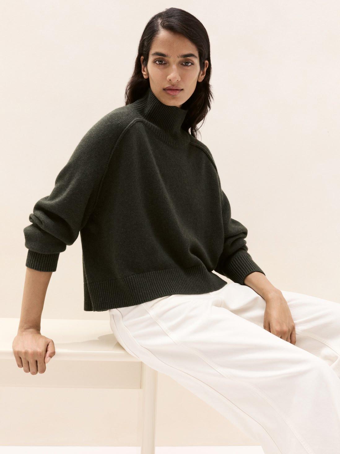 a woman sitting on a white bench wearing a green sweater